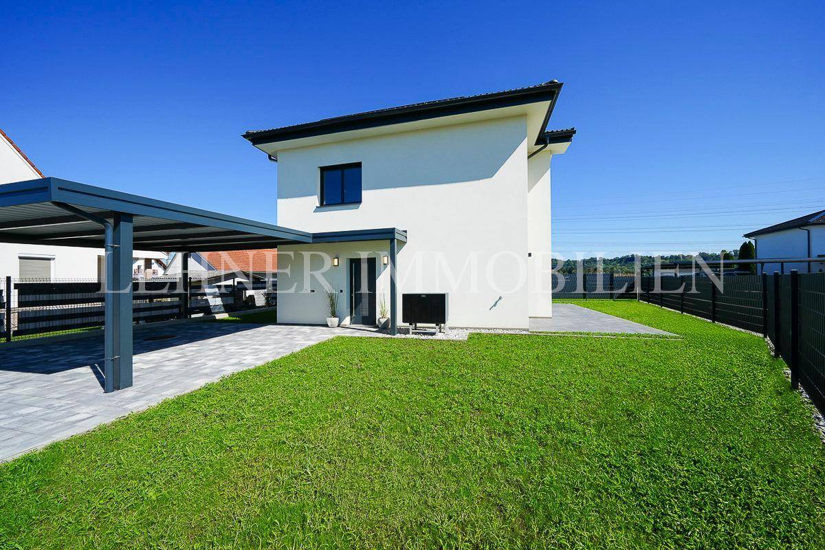 Seitenansicht des Hauses mit modernem Carport und gepflasterter Zufahrt, umgeben von gepflegten Grünflächen.