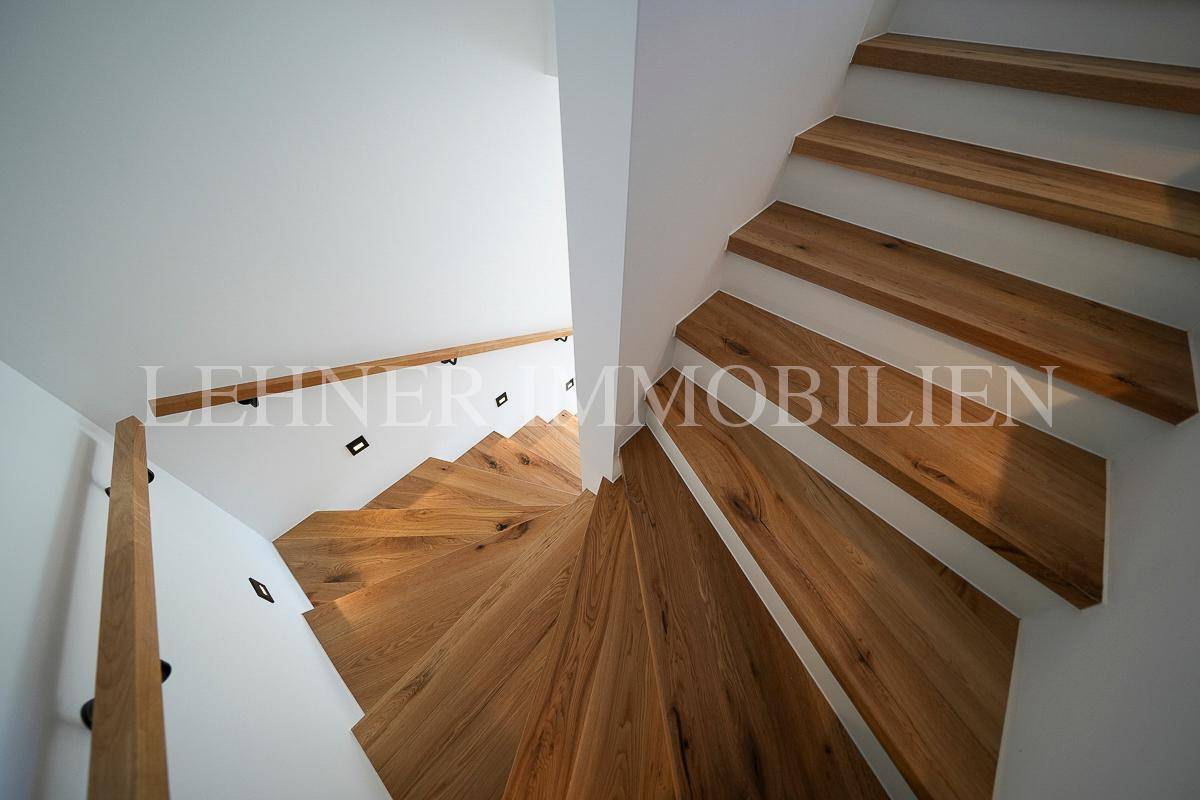 Wendeltreppe aus hellem Holz mit minimalistischem Geländer und integrierter Wandbeleuchtung.