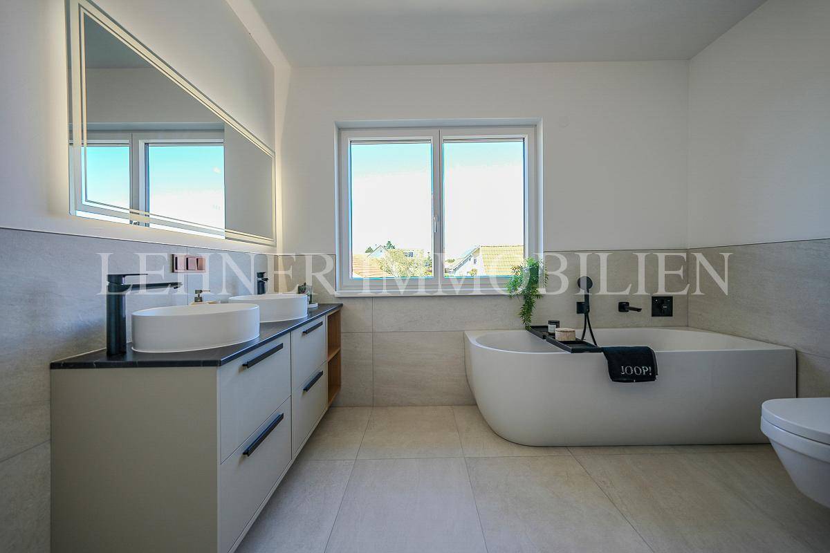 Geräumiges Badezimmer mit Doppelwaschbecken, beleuchtetem Spiegel und freistehender Badewanne.
