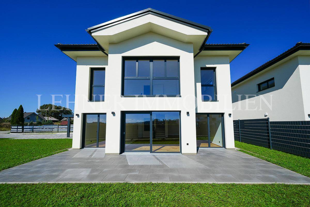 Frontansicht des modernen Hauses mit großen Fensterfronten und einer einladenden Terrasse zum Garten hin ausgerichtet.