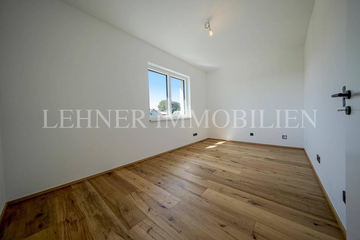 Helles, leeres Zimmer mit neuem Holzparkettboden und einem Fenster mit Blick ins Grüne.