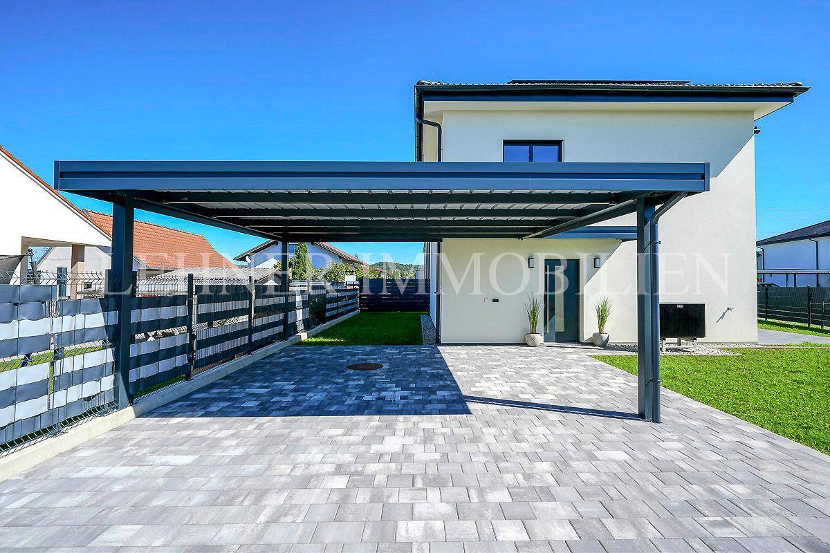 Geräumiger Carport mit moderner Überdachung und gepflastertem Bereich vor dem Hauseingang, bietet Schutz für Fahrzeuge.