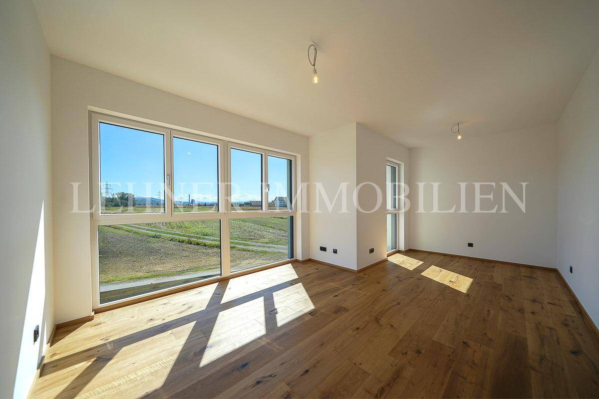 Lichtdurchfluteter Raum mit großen Fenstern, Holzboden und weitem Blick ins Grüne.