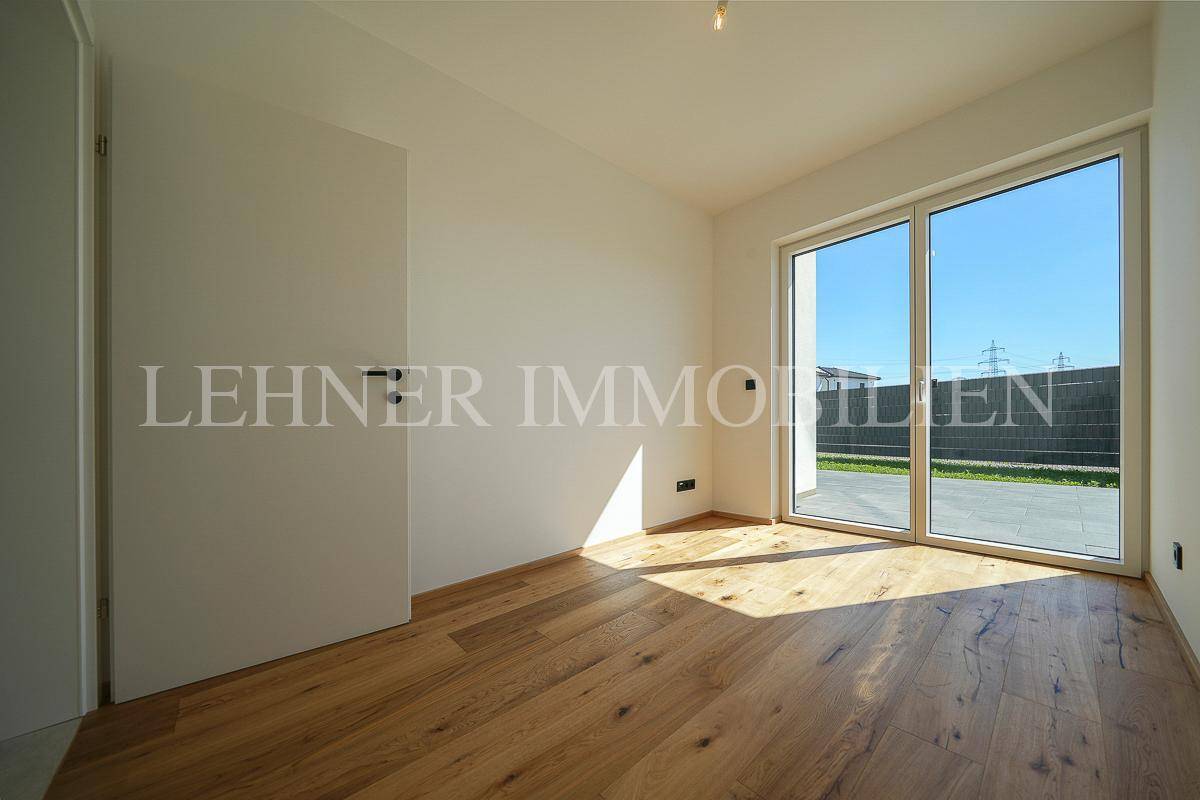 Helles Zimmer mit Parkettboden und großen Fenstern, die Zugang zum Außenbereich ermöglichen und viel Licht spenden.