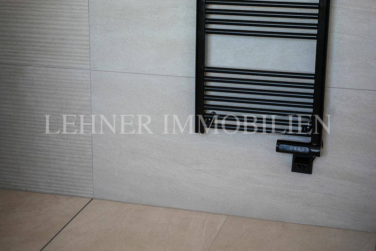 Schwarzer beheizter Handtuchhalter an der Wand im modern gestalteten Badezimmer.