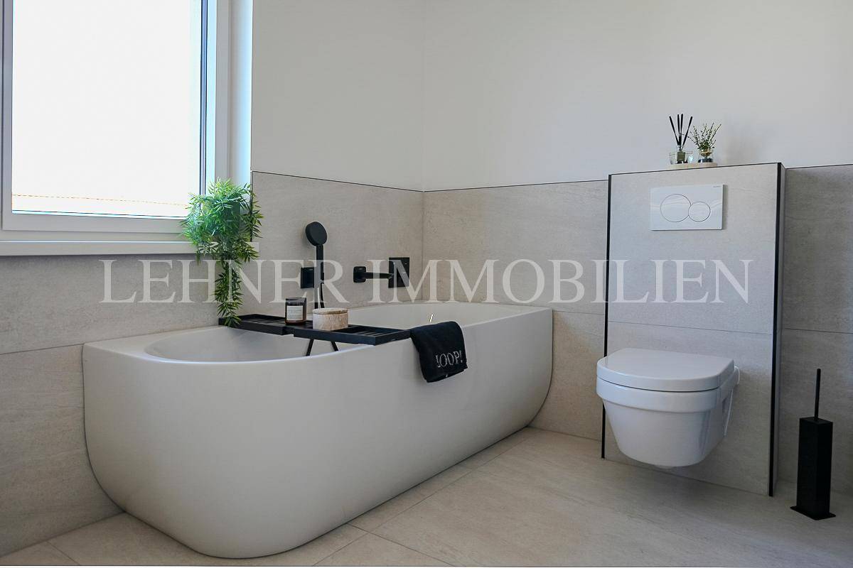 Freistehende Badewanne und Wand-WC in einem hell gefliesten, modernen Badezimmer.