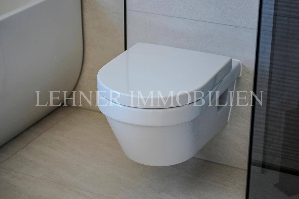 Modernes Wand-WC neben der Badewanne in einem hell gefliesten Badezimmer.