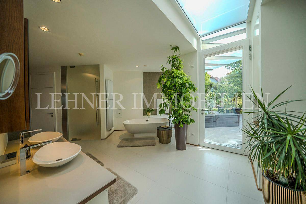 Helles Badezimmer mit Doppelwaschbecken, Badewanne und Zugang zum Außenbereich.