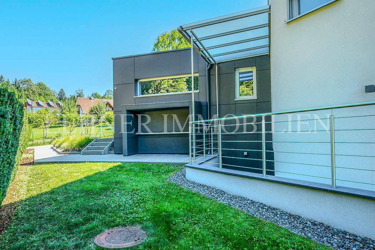 Moderne Gebäudefassade mit integrierter Garage, gepflegtem Rasen und grüner Hecke.