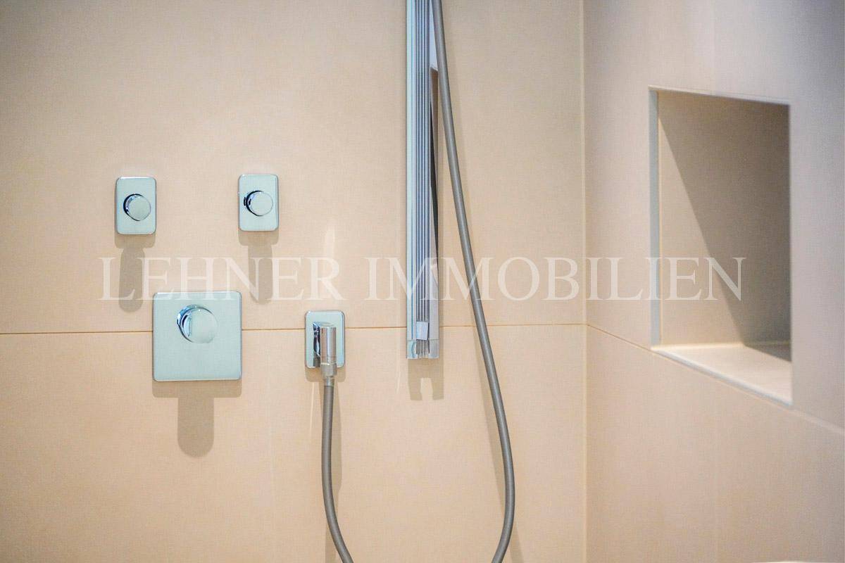 Moderne Duscharmaturen und Handbrause in einem elegant gefliesten Duschbereich.