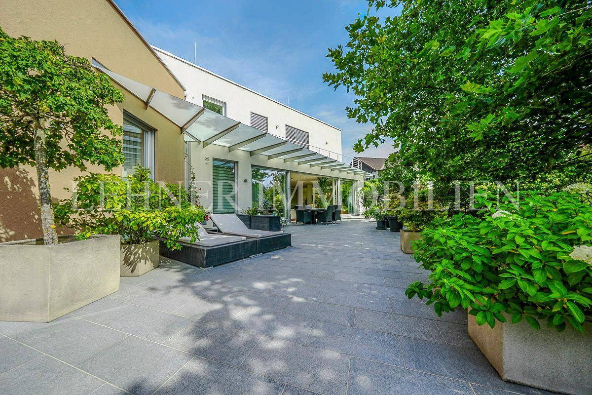 Geräumige Steinterrasse mit modernen Lounge-Möbeln und Blick auf den Garten und die Umgebung.