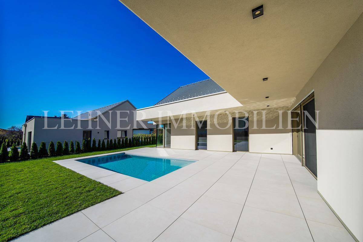 Weitläufiger Gartenbereich mit modernem Haus, Pool und großer Terrasse unter strahlend blauem Himmel.
