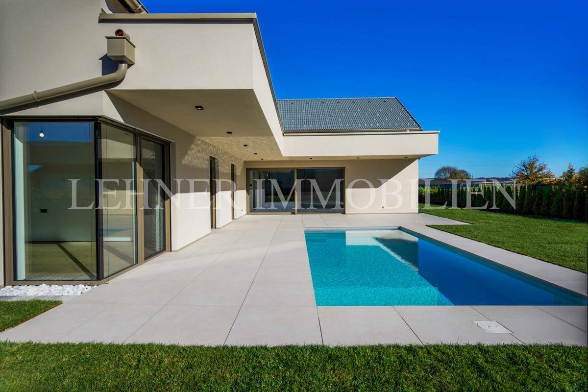 Ansicht des modernen Hauses mit Pool und heller Terrasse, umgeben von gepflegtem Rasen.