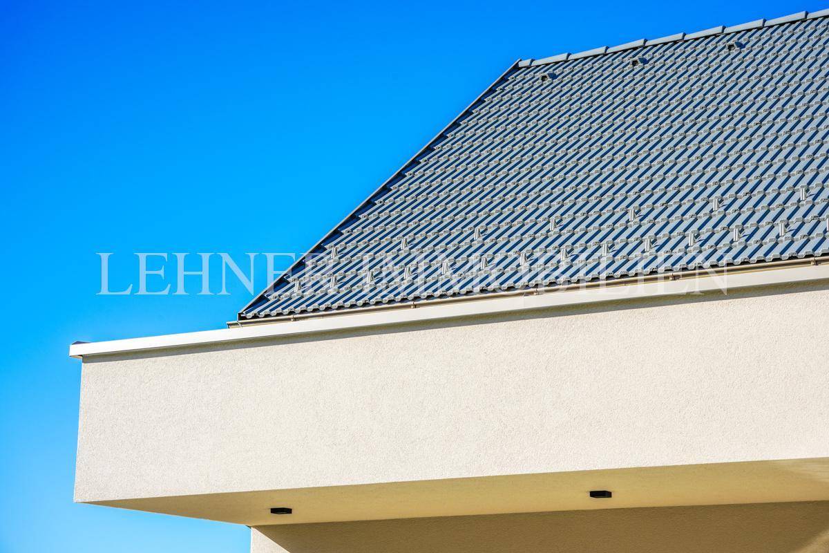 Detailansicht eines modernen Daches mit Ziegeln und weißer Fassade unter blauem Himmel.