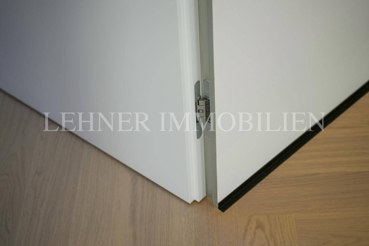 Detailaufnahme einer modernen weißen Tür mit sichtbarem Scharnier und Parkettboden.