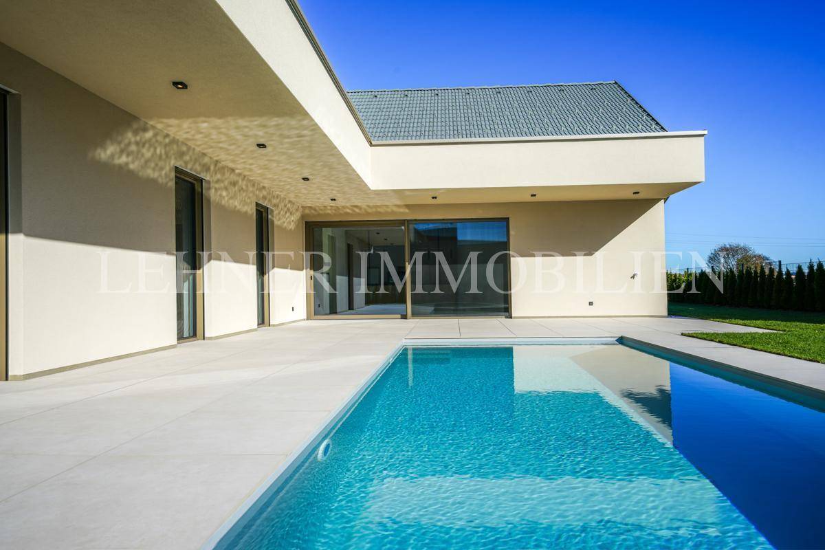 Sonniger Außenbereich des modernen Hauses mit erfrischendem Pool und heller Terrasse unter blauem Himmel.