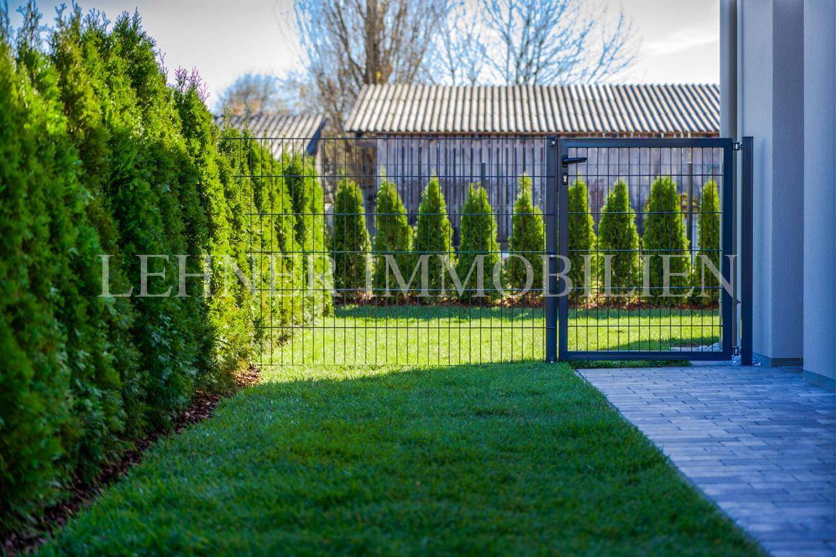 Gepflegter Gartenbereich mit modernem Zaun, Tor und dichter Hecke.
