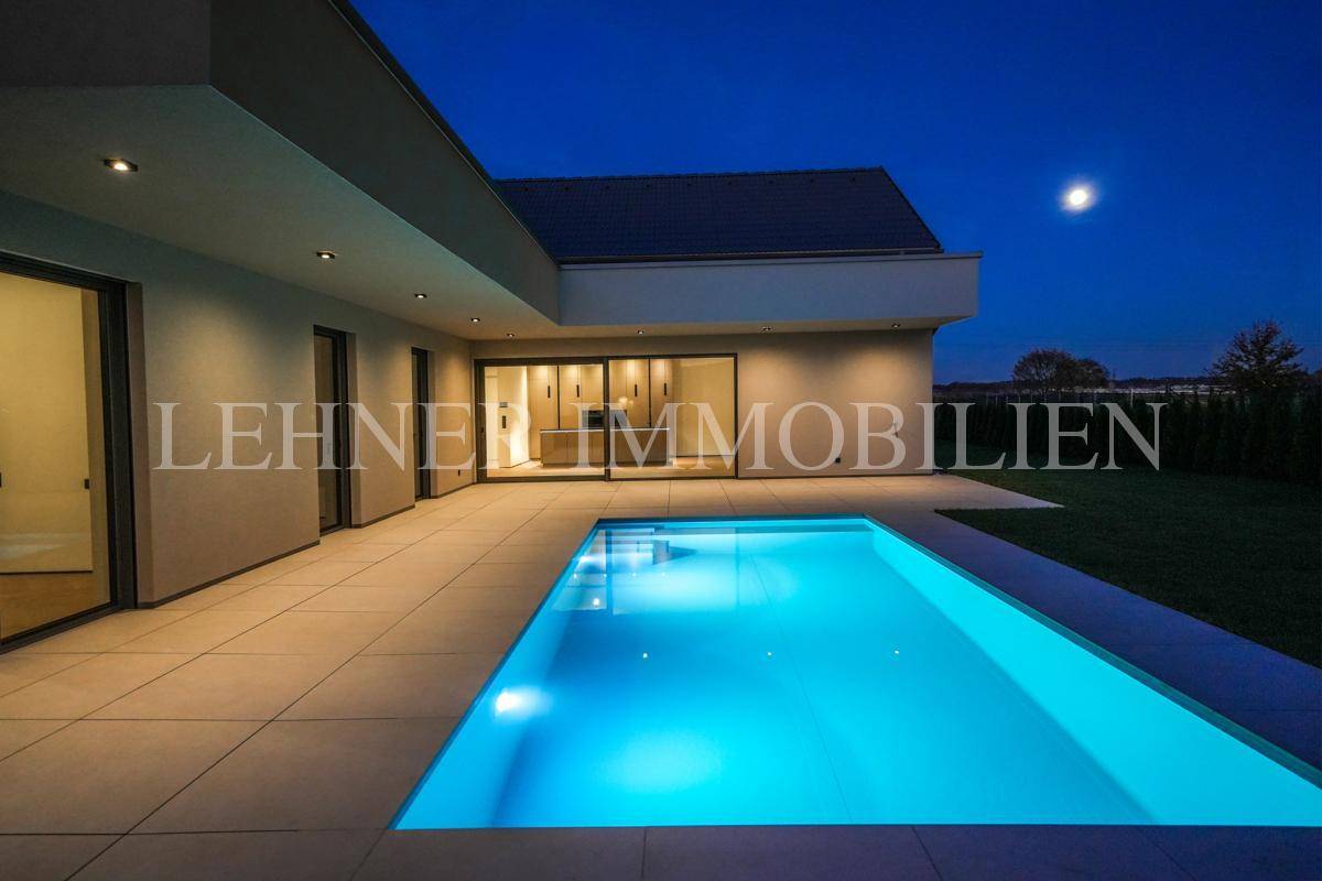 Elegantes Haus bei Dämmerung mit leuchtendem Poolbereich und weitläufiger Terrasse.