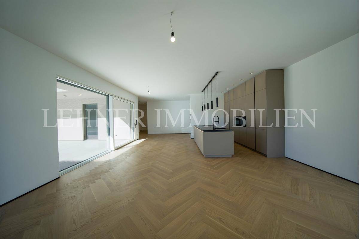 Weitläufiger Wohnbereich mit moderner Küche, Fischgrätparkett und Zugang zur Terrasse durch Schiebetüren.