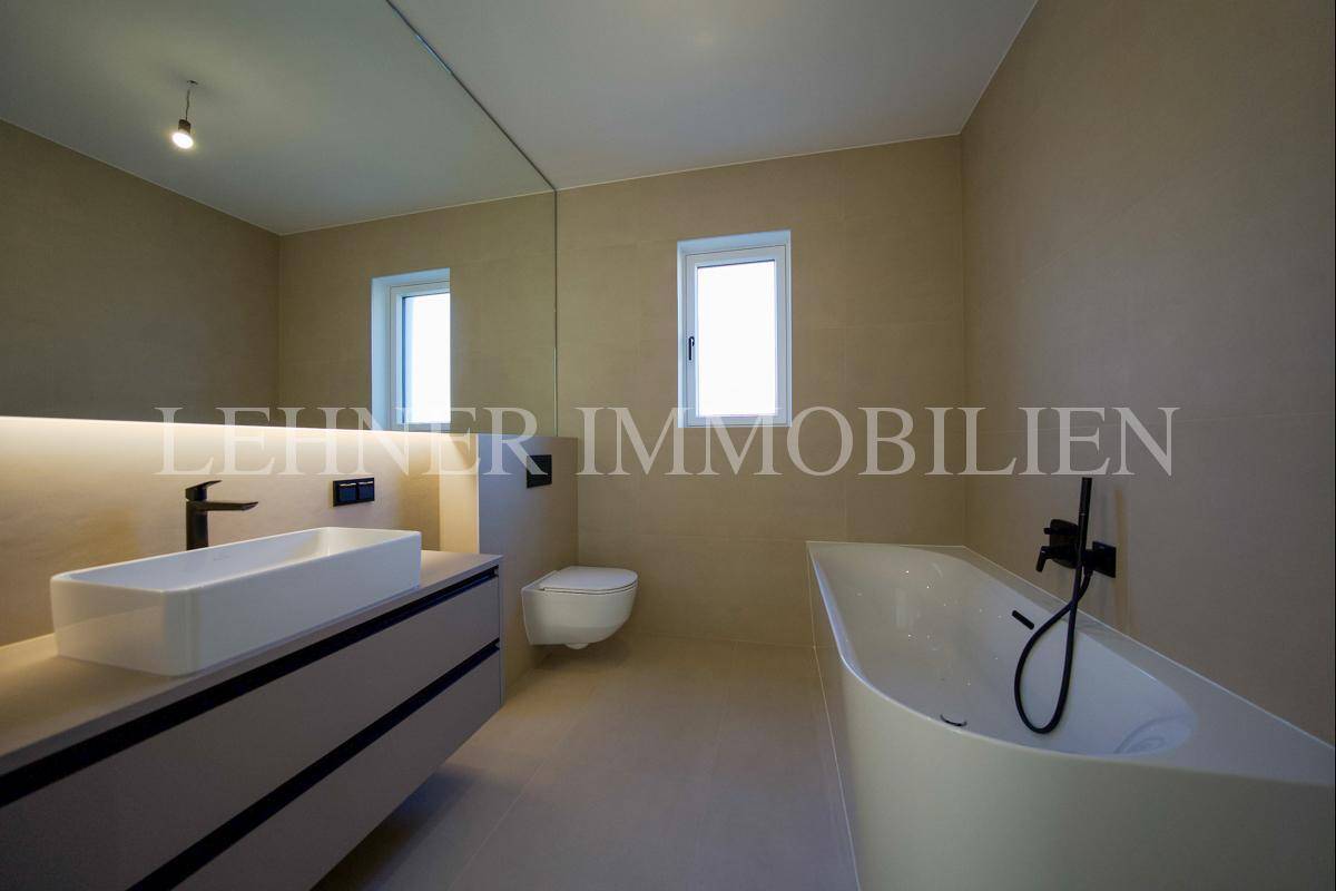 Modernes Badezimmer mit beigefarbenen Fliesen, rechteckigem Waschbecken, Badewanne und Fenster.
