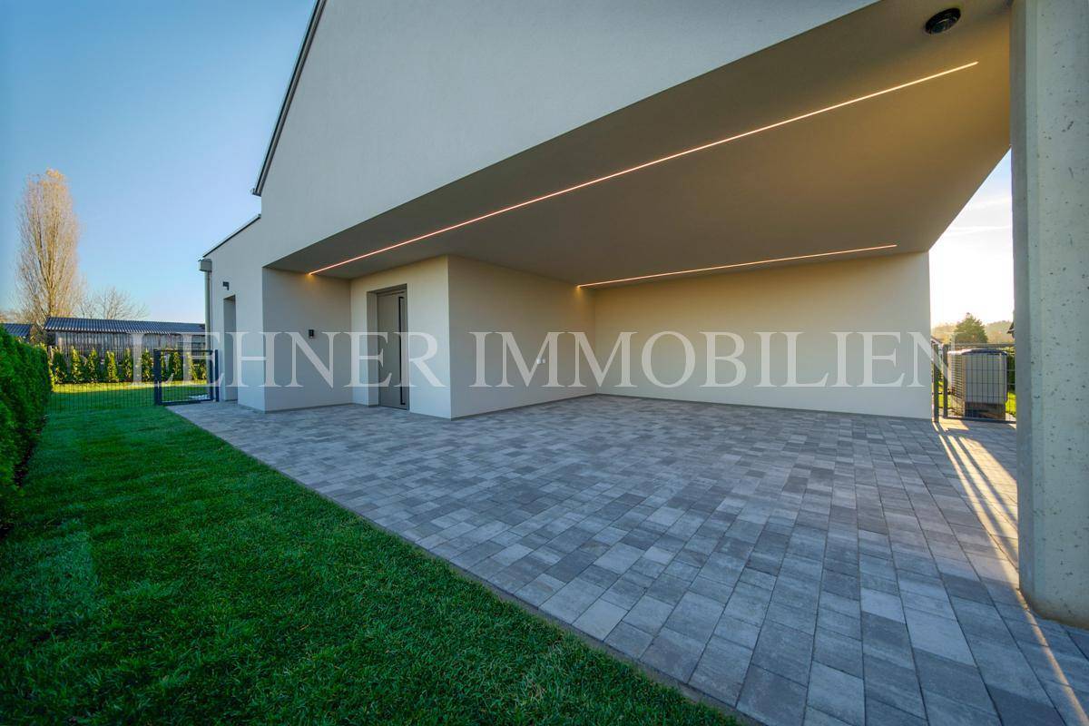 Heller Carport-Bereich mit moderner Beleuchtung und gepflasterter Fläche an einem sonnigen Tag.