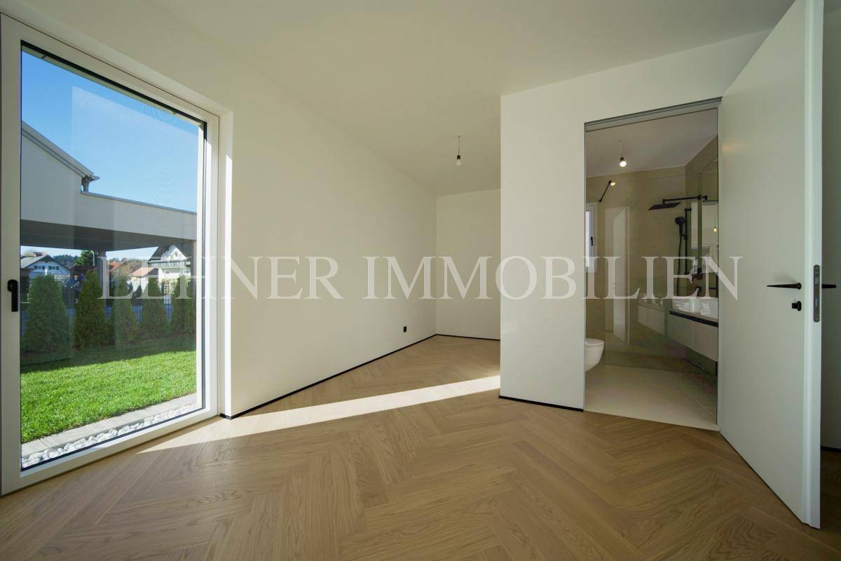 Schlafzimmer mit Holzboden und direktem Zugang zu einem modernen Badezimmer.