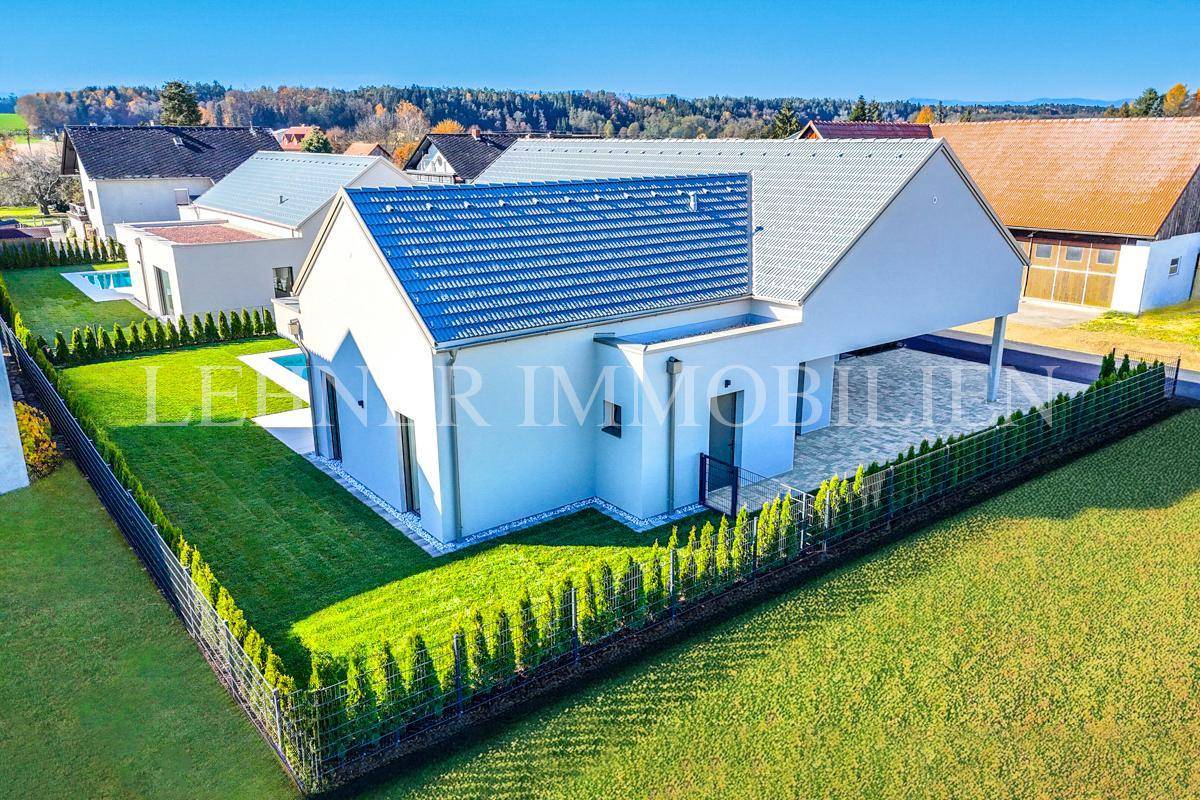 Gesamtansicht des modernen Anwesens mit gepflegtem Garten, Zaun und umliegender Bebauung.