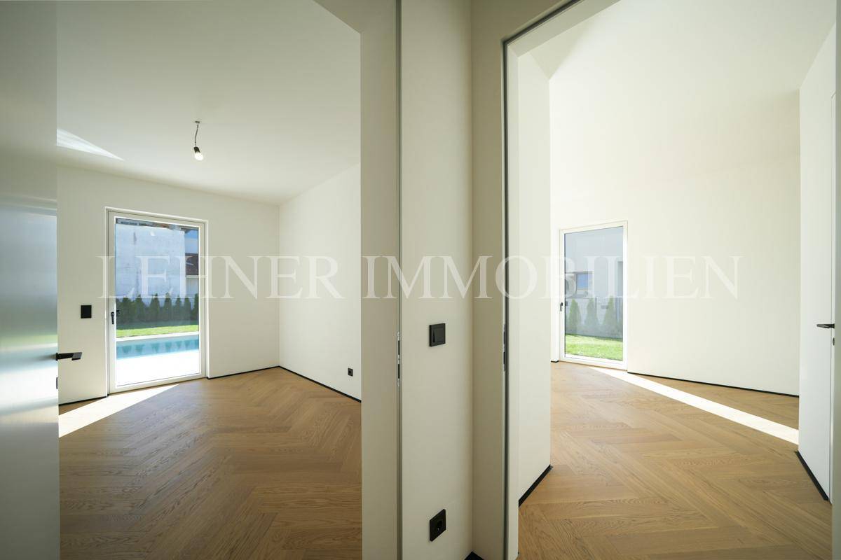 Helles Zimmer mit Holzboden und Zugang zu einem Außenbereich mit Poolblick.