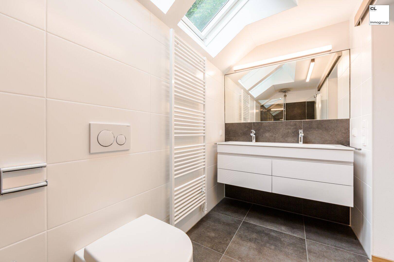 Modernes Badezimmer mit weißen Fliesen, dunklem Boden und einem Dachfenster für natürliches Licht.