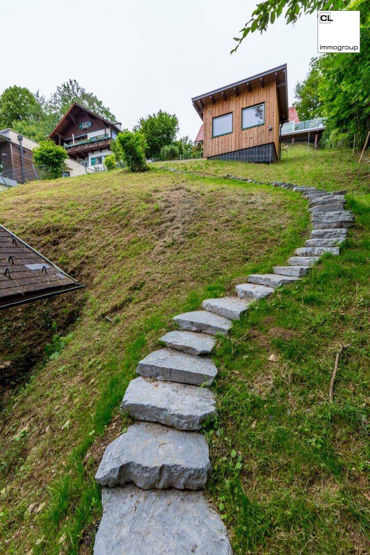 Geschwungener Steinweg führt einen grünen Hügel hinauf zu einem Holzhaus.