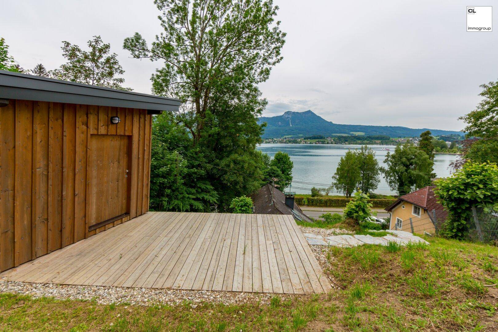 Geräumige Holzterrasse auf einem Hügel mit Panoramablick auf den See und die Berge.
