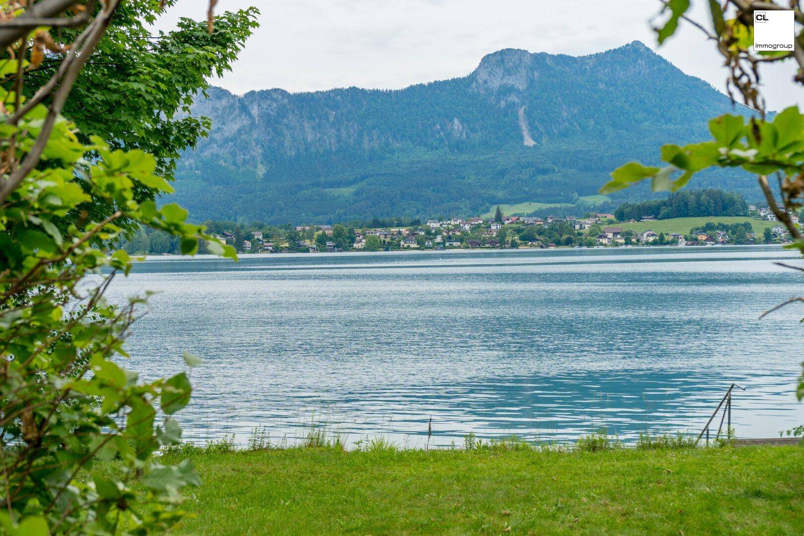 Weitläufiger Blick auf den ruhigen See, die majestätischen Berge und ein Dorf am Ufer.