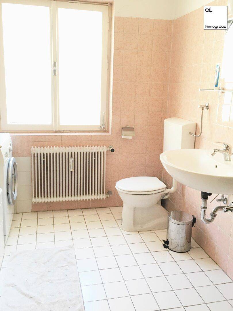 Badezimmer mit Badewanne, Waschbecken, WC und Fenster, ausgestattet mit rosa Fliesen.