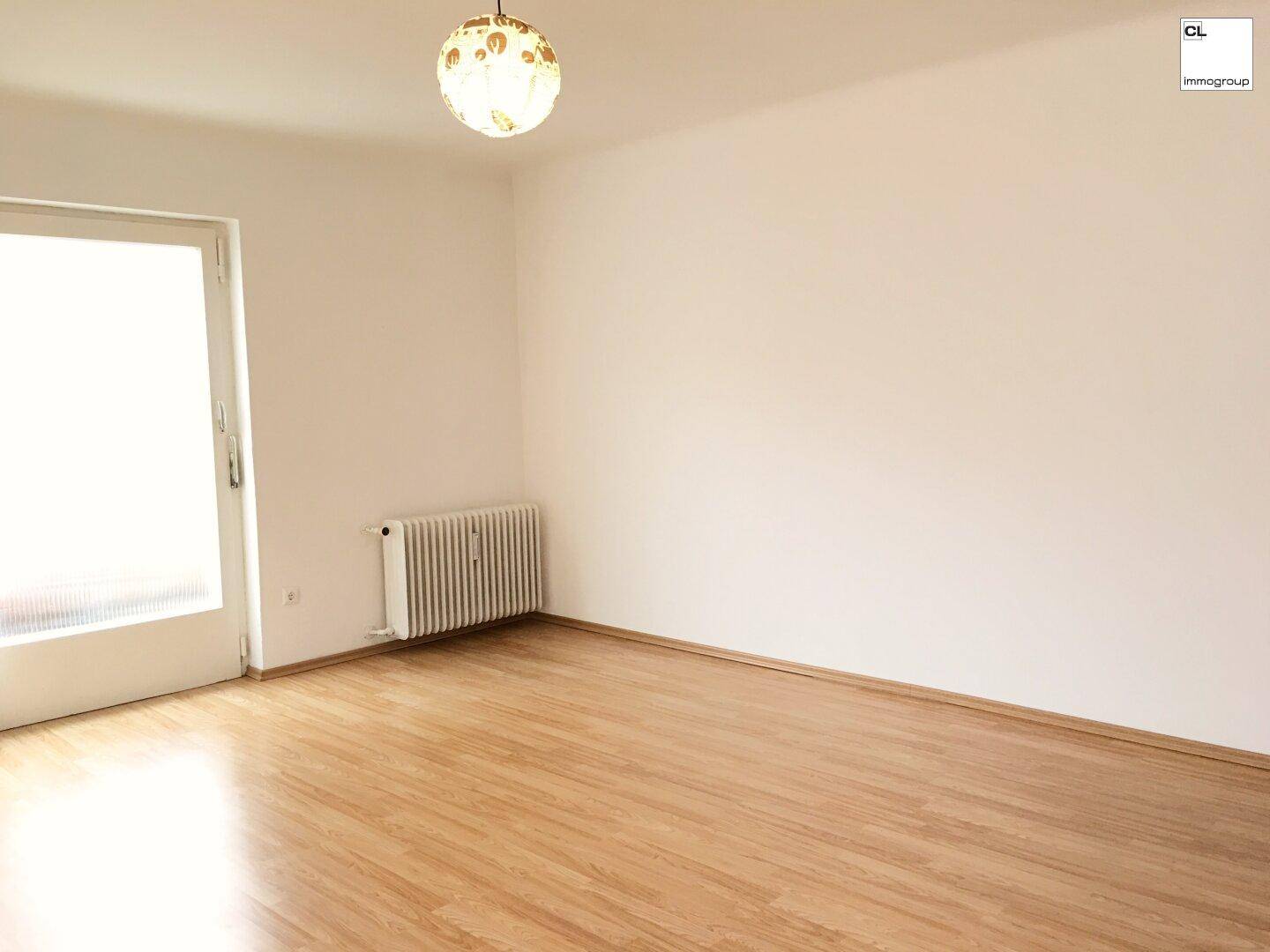 Leeres Zimmer mit Laminatboden, Heizkörper und Fenster, bereit zur individuellen Gestaltung.