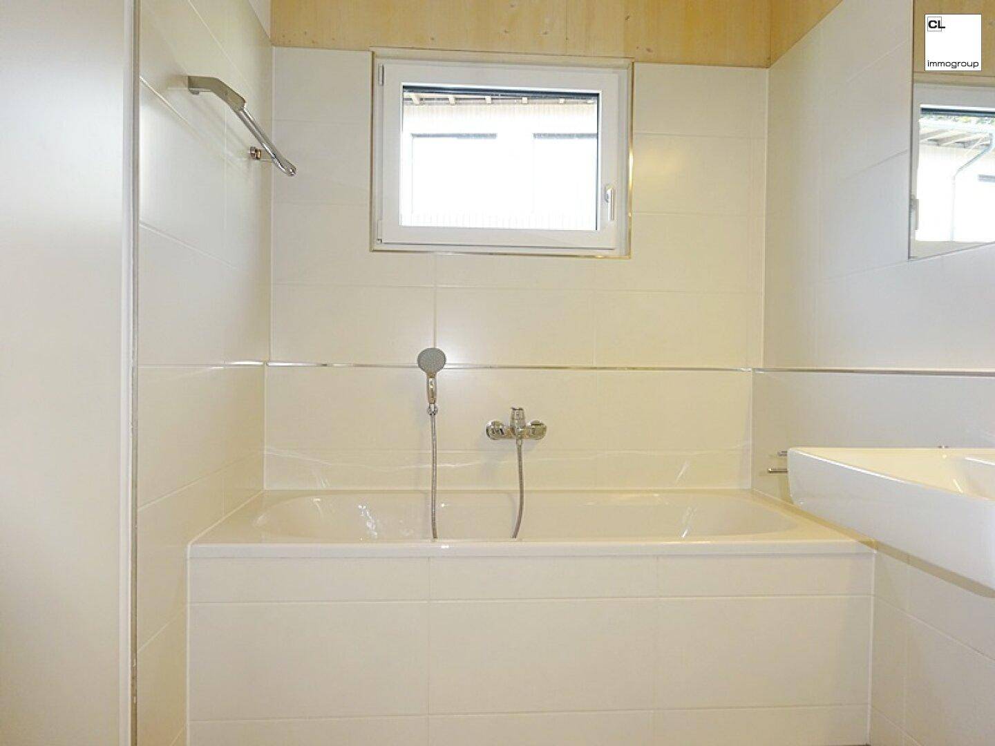 Helles Badezimmer mit Badewanne, Einzelwaschbecken und Fenster für Tageslicht.