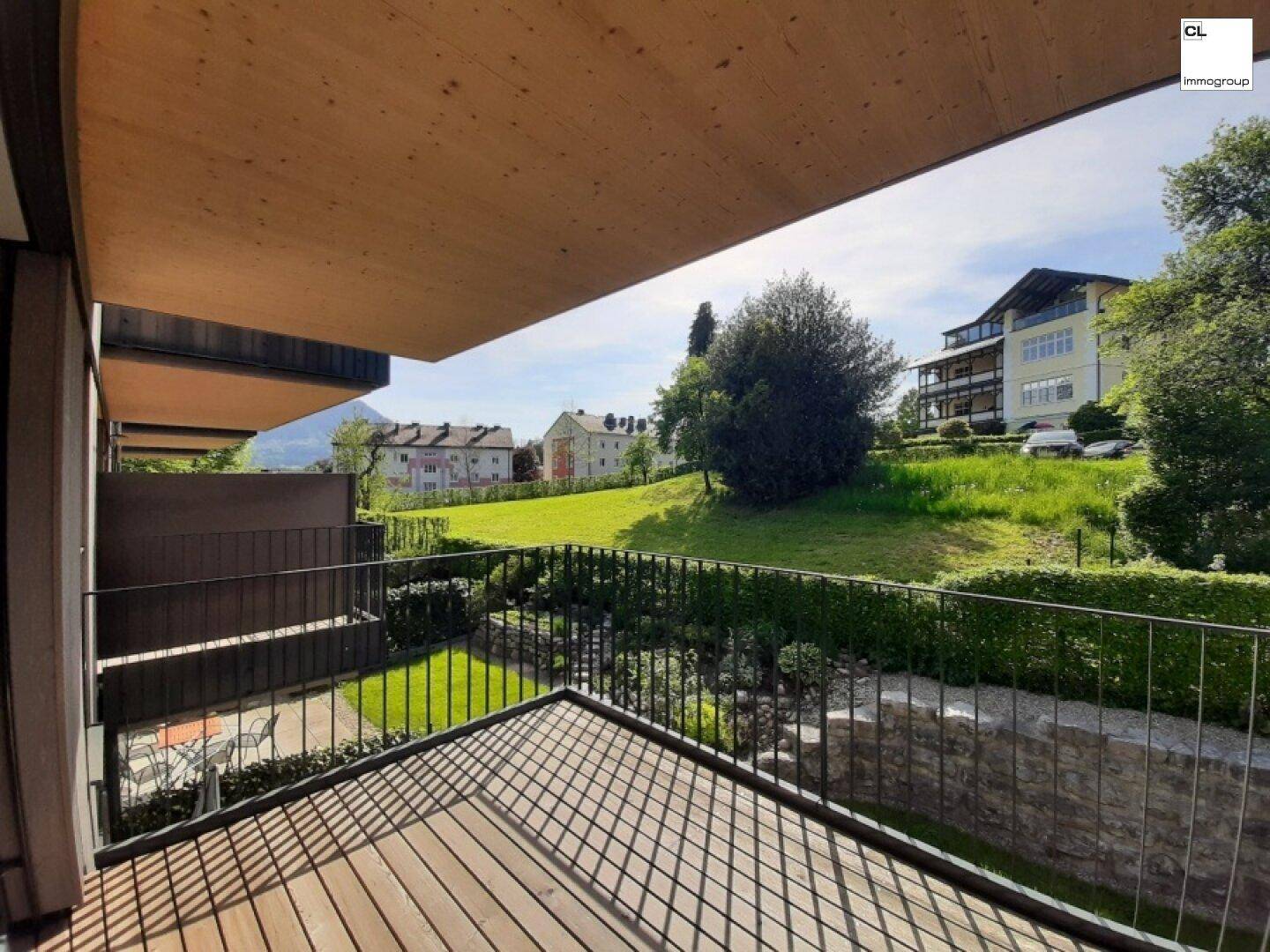 Geräumiger Balkon mit Holzboden und freiem Blick auf die grüne Umgebung und Gebäude.