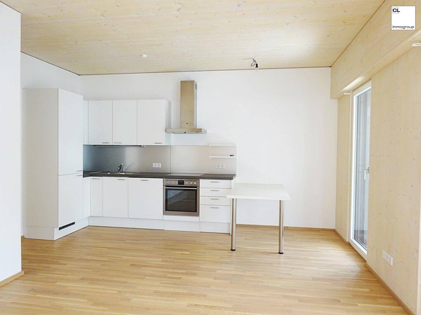 Moderne weiße Einbauküche in einem hellen Raum mit Holzboden und Holzbalkendecke.