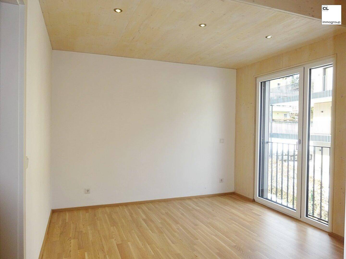 Helles Schlafzimmer mit Holzboden, Holzbalkendecke und Zugang zu einem französischen Balkon.