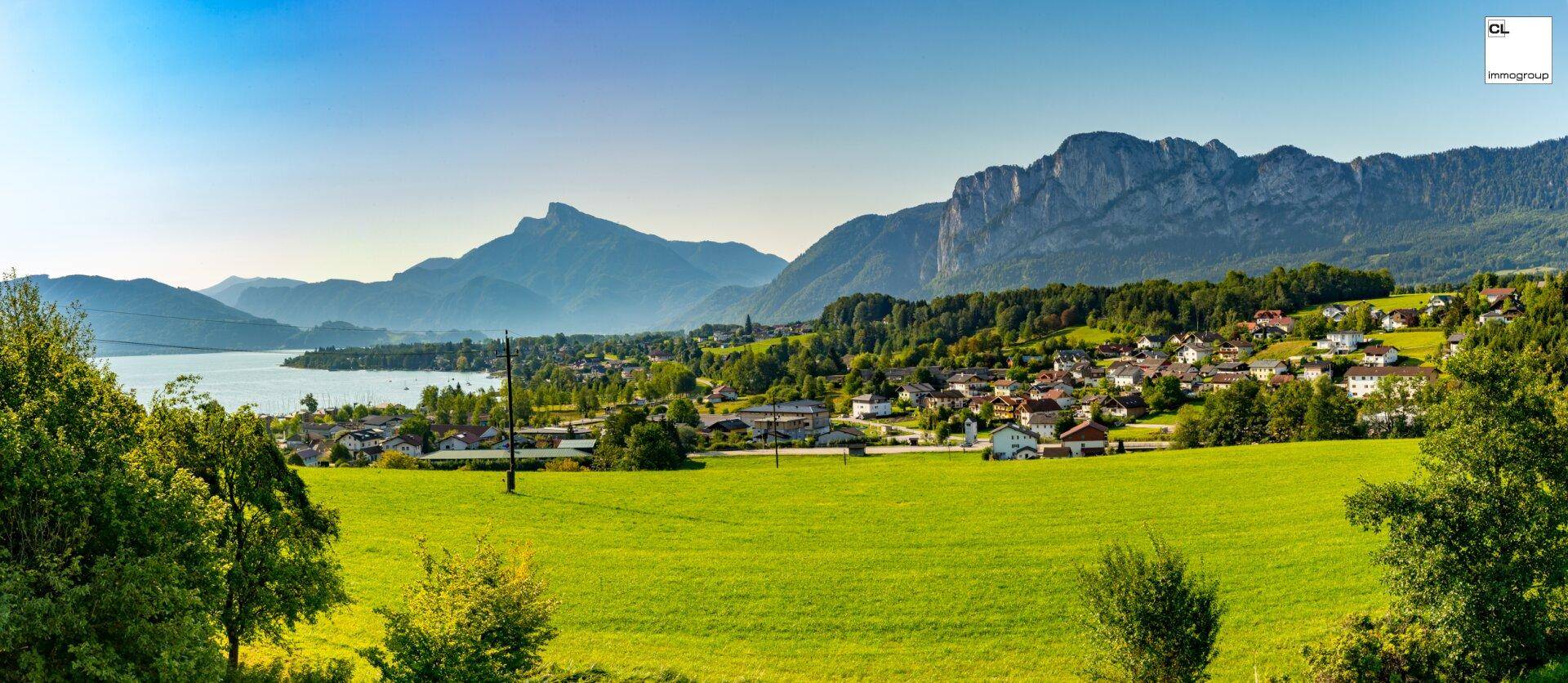 Panoramablick über eine malerische Landschaft mit See, Bergen und einem charmanten Dorf.