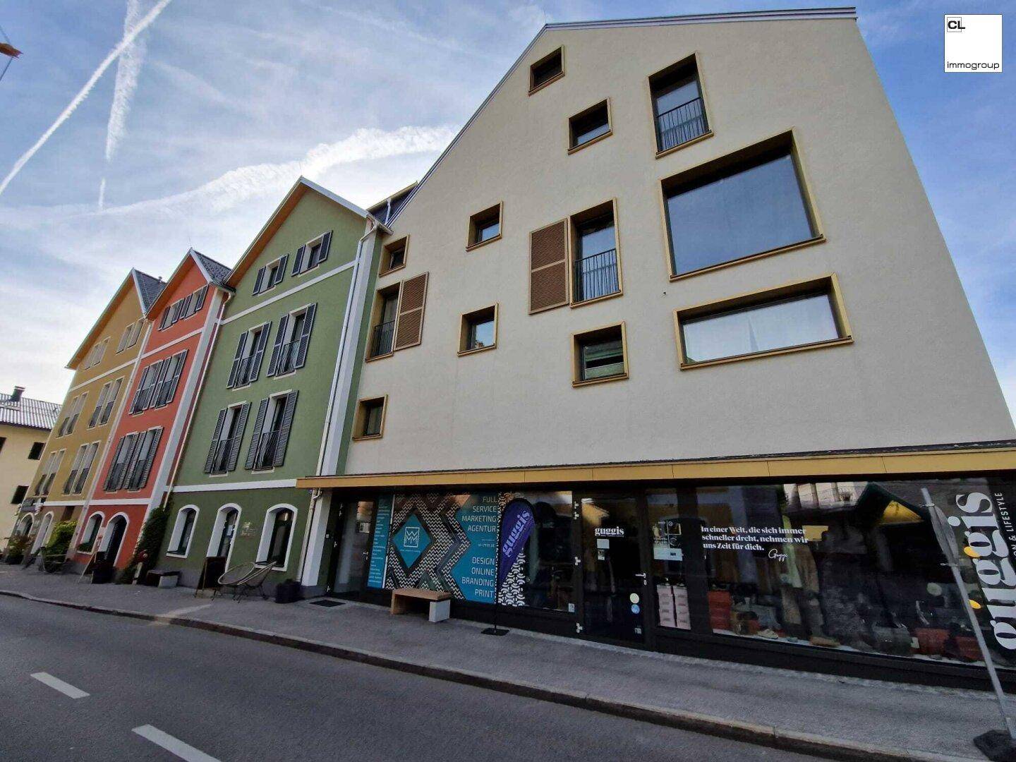 Moderne Gebäudefassade mit unregelmäßigen Fenstern und Geschäften im Erdgeschoss.