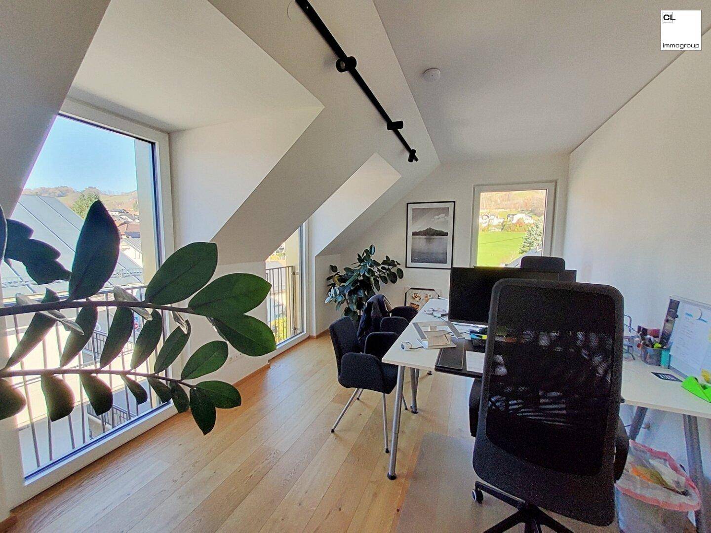 Helles Büro im Dachgeschoss mit Holzboden, Dachschrägen und weitem Blick ins Grüne.