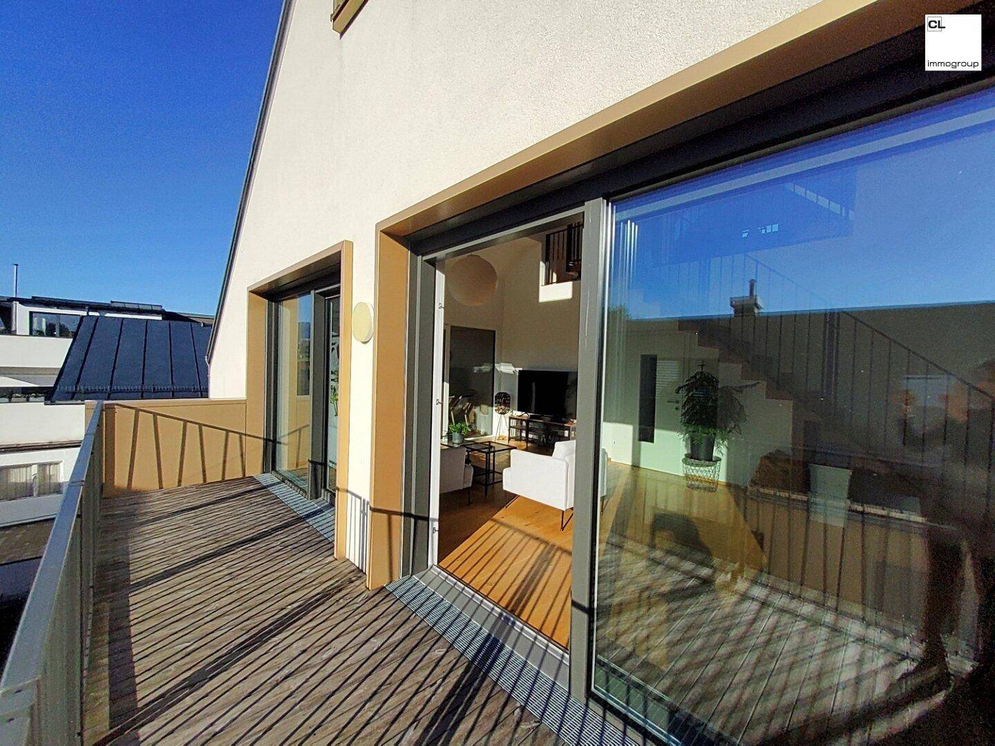 Heller Balkon mit Holzboden und großen Schiebetüren zum lichtdurchfluteten Innenbereich.