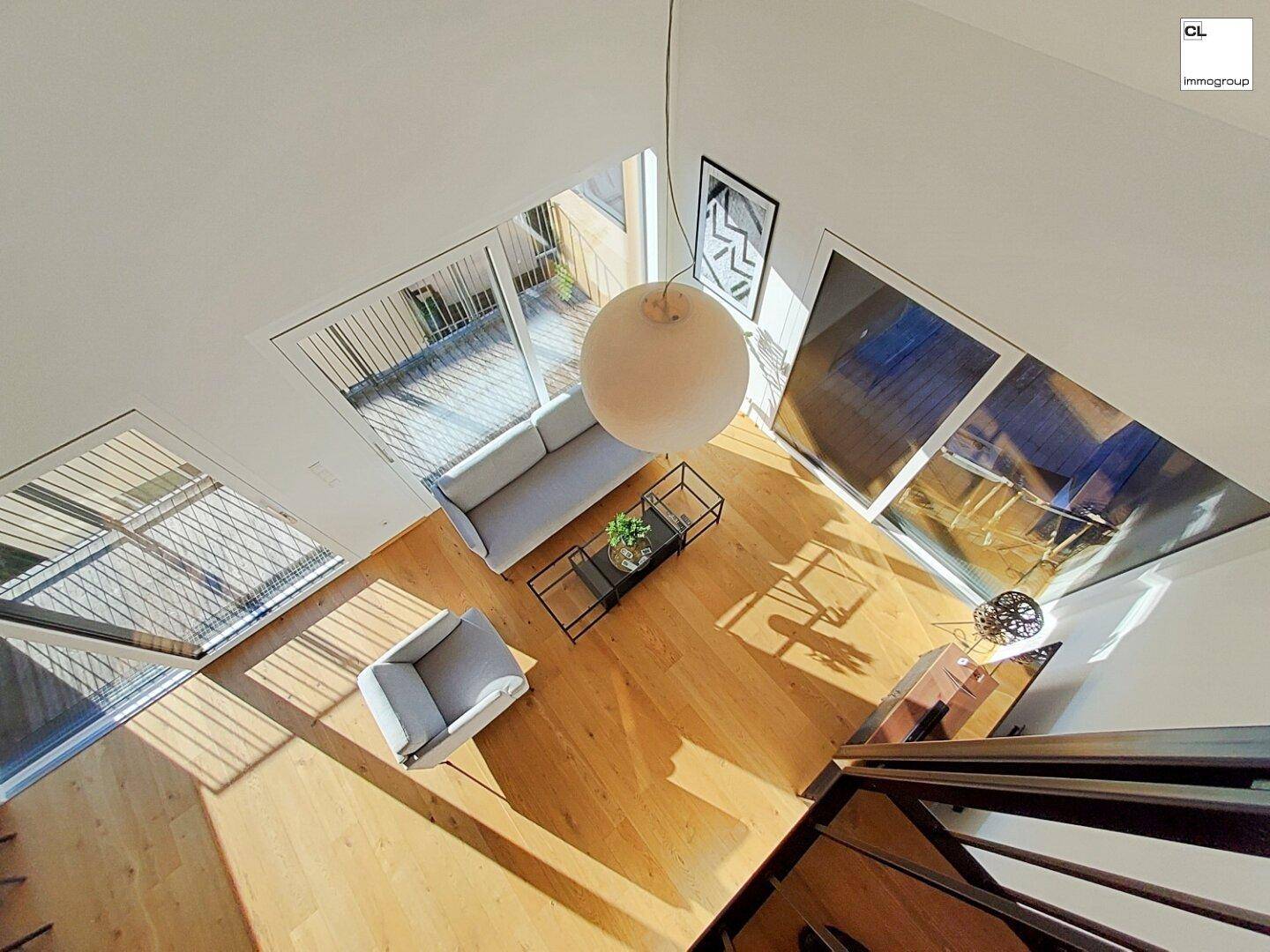 Lichtdurchfluteter Wohnbereich mit hohen Decken, Holzboden und Blick auf die Terrasse.