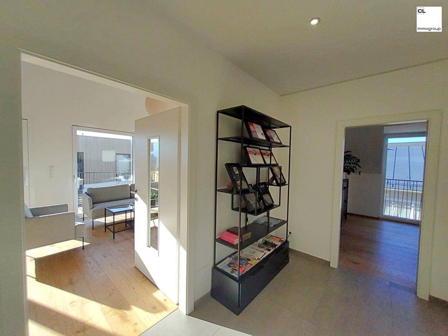 Heller Eingangsbereich mit Holzboden und Blick in den offenen Wohnbereich und auf den Balkon.