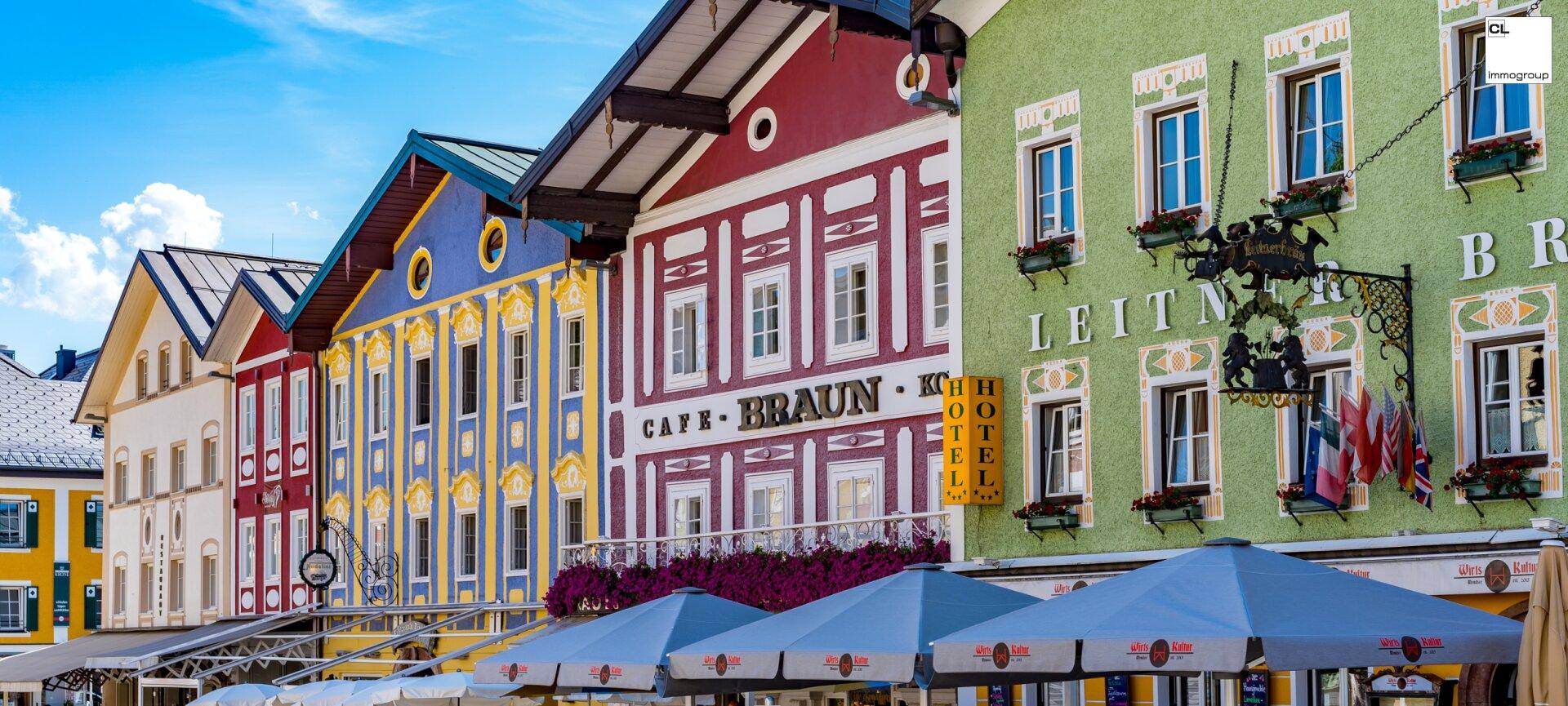 Reihe farbenfroher traditioneller Gebäude mit kunstvollen Fassaden und Blumenkästen unter strahlendem Himmel.