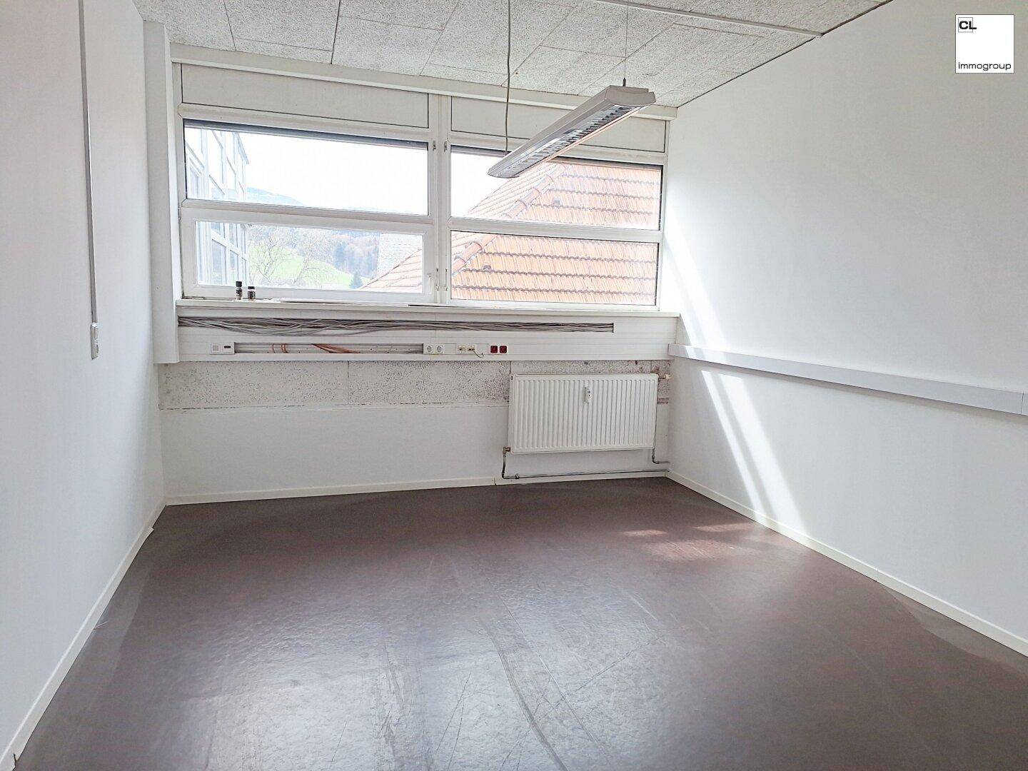 Kleiner, heller Büroraum mit großen Fenstern, die viel Tageslicht hereinlassen, und einem Heizkörper.