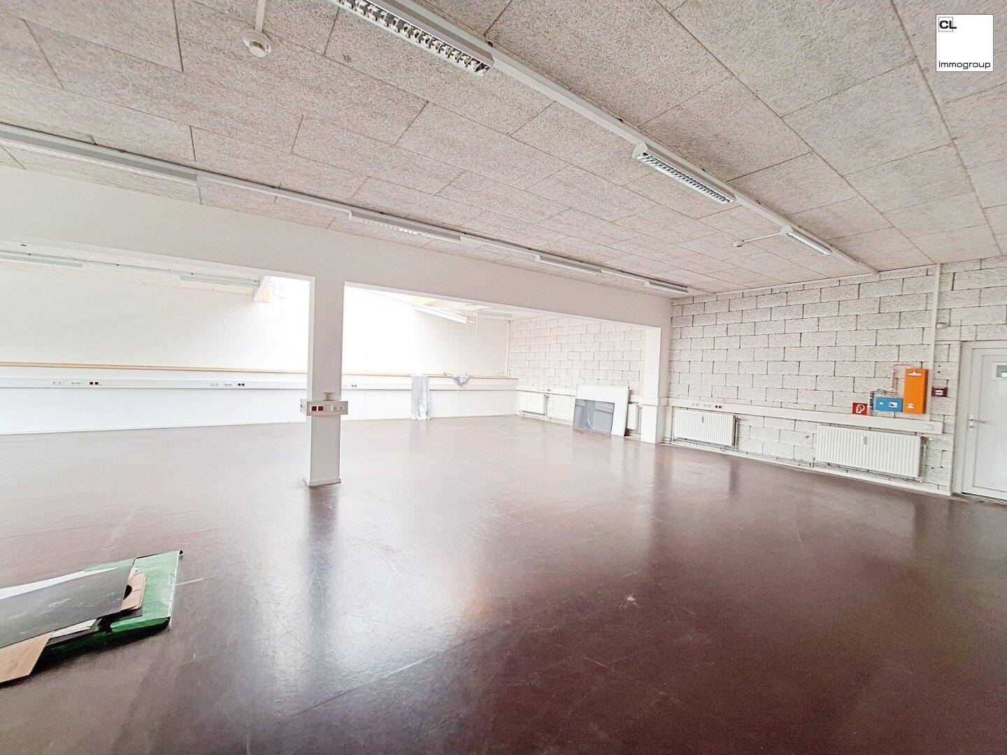 Geräumiger Gewerberaum mit Betonboden, weißen Wänden und einer Ziegelwand, ideal für verschiedene Nutzungen.