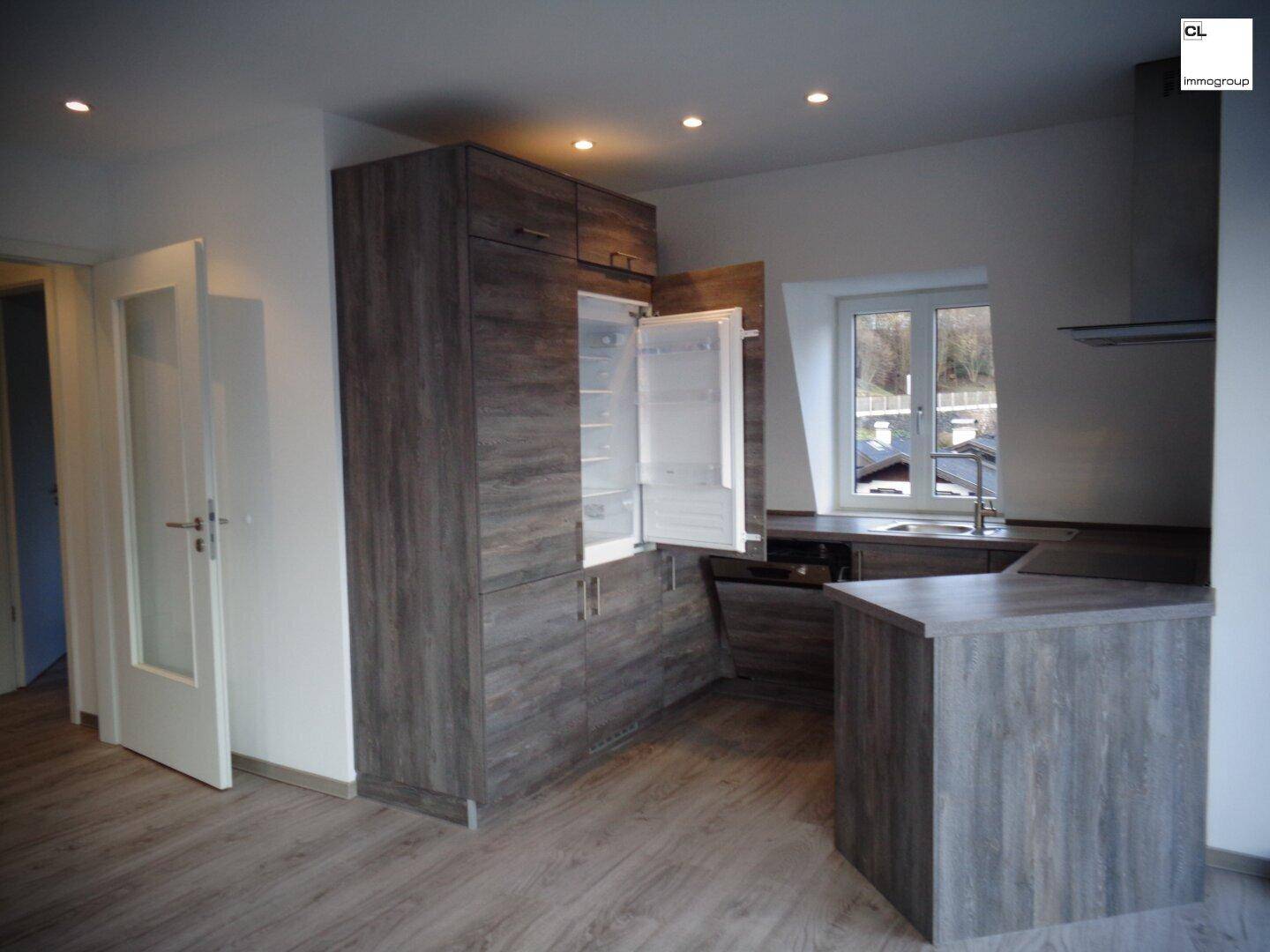 Funktionale Küche mit Holzoptik-Schränken, integriertem Kühlschrank und Fenster.