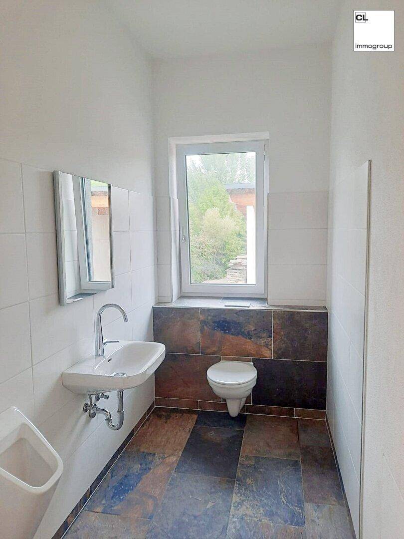 Helles Badezimmer mit modernem Design, Urinal, Toilette und Fenster, ausgestattet mit Fliesen.