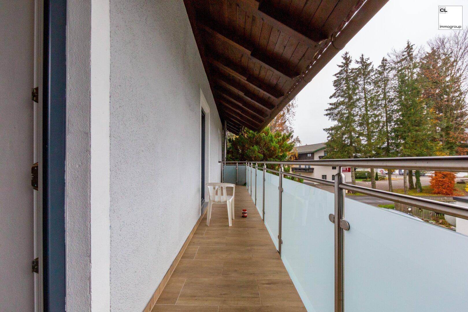 Langer Balkon mit Fliesenboden, Glasgeländer und Blick ins Grüne.